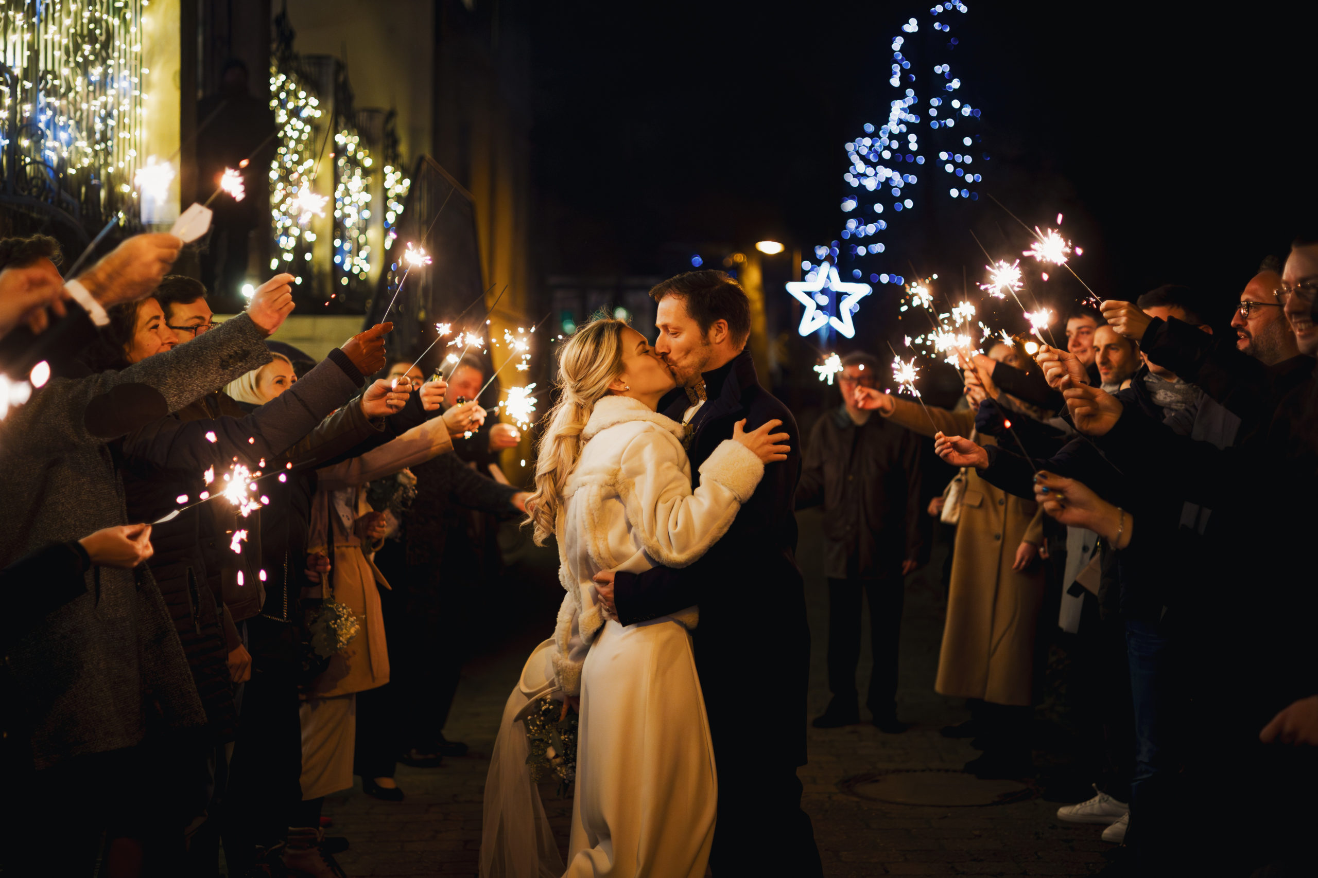 les mariés s'embrassant au milieu de leurs invités qui tiennent des cierges magiques